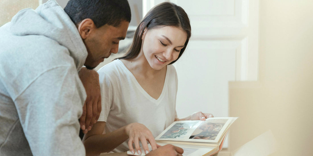 Smiling couple flipping through a family photo album together at home, looking at prints they want to preserve
