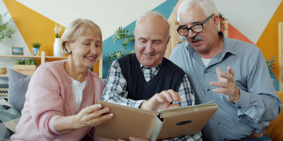 Three older adults sitting together on a couch, smiling as they look through a photo album.