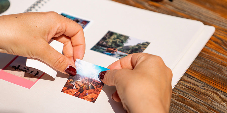A close-up of hands peeling a small canyon landscape photo off a sticky album page.