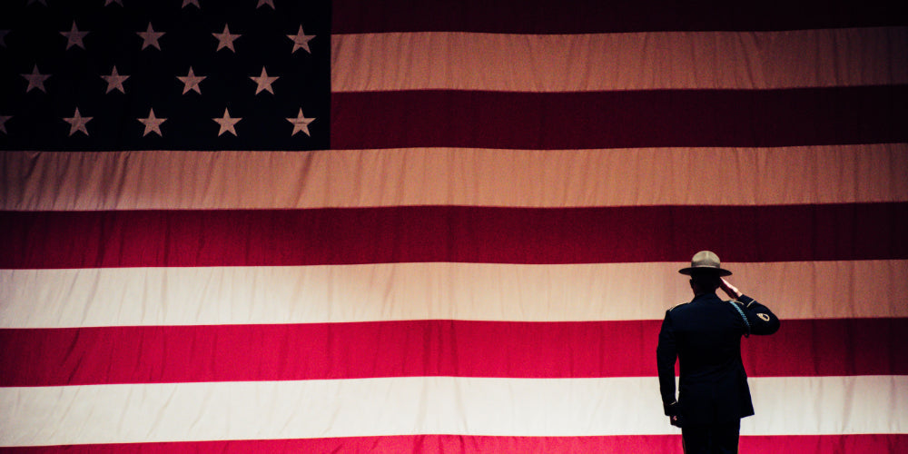 Silhouette of a soldier in dress uniform and campaign hat saluting a large American flag