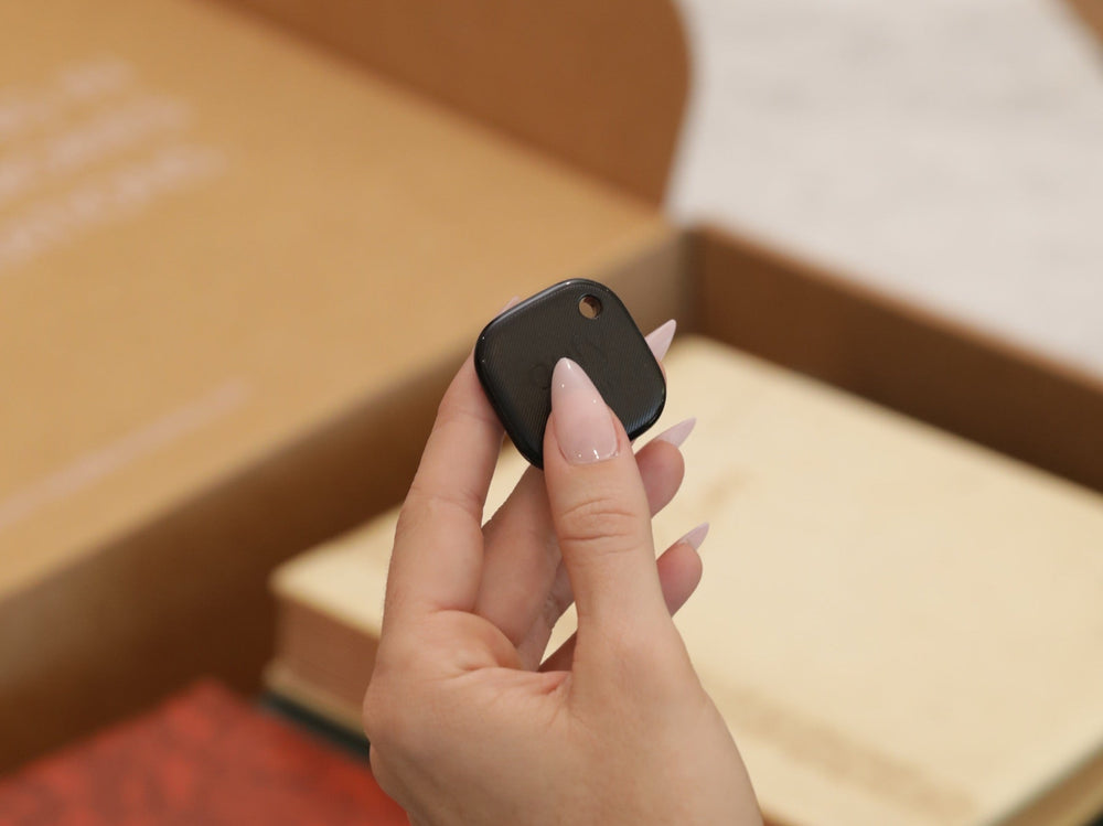 A hand holding the Photokive AirTracker over albums packed in a shipping box