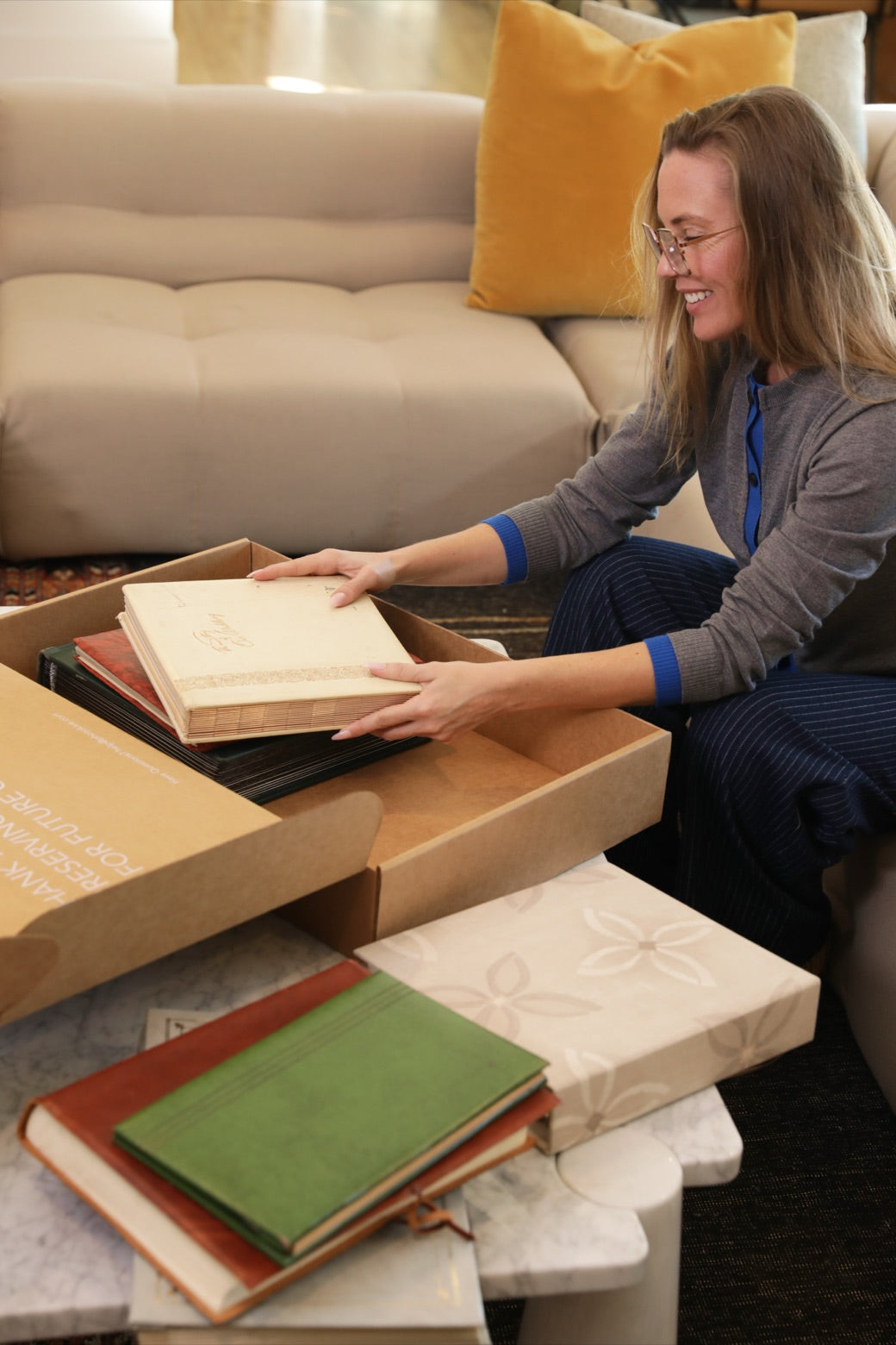 A woman packing vintage family photo albums into a Photokive shipping box at home