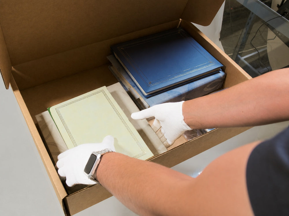 Gloved hands carefully packing family albums into a Photokive archival box